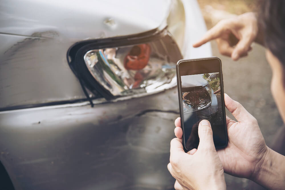 Eine Person fotografiert nach einem Autounfall mit dem Smartphone einen beschädigten Autoscheinwerfer und die Stoßstange