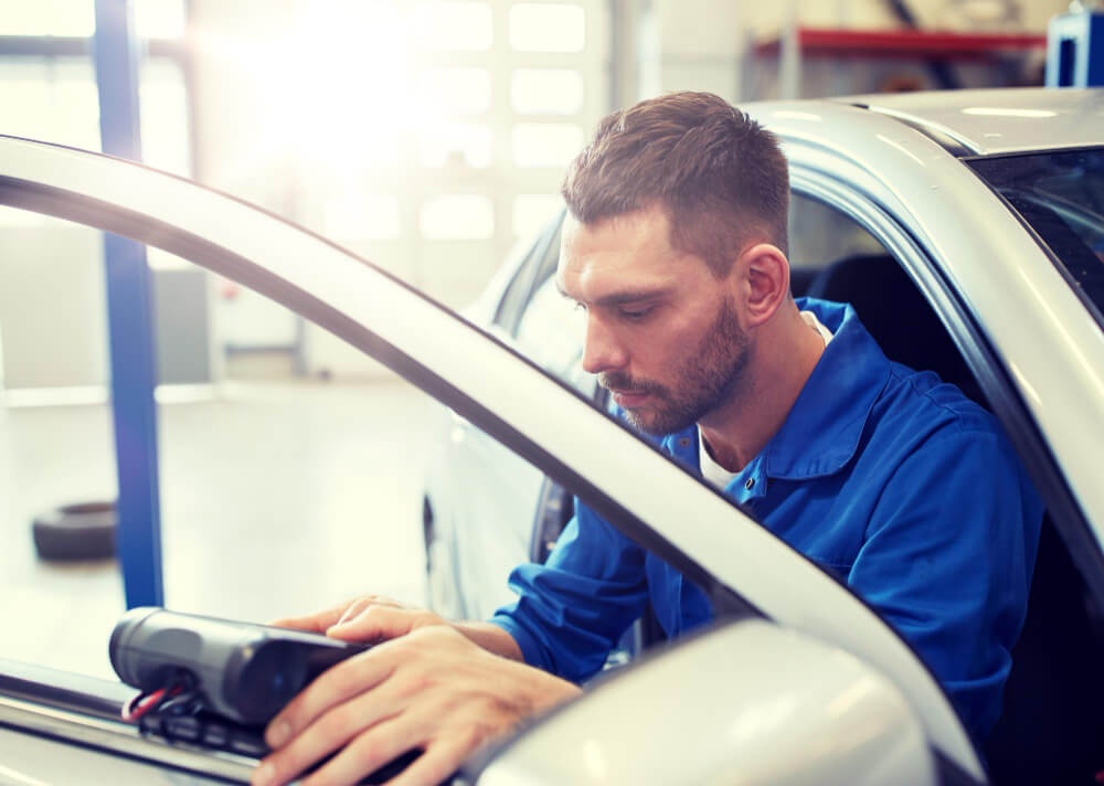 Ein Mechaniker im blauen Overall nutzt ein Diagnosegerät für ein Unfallgutachten im Auto in einer Werkstatt