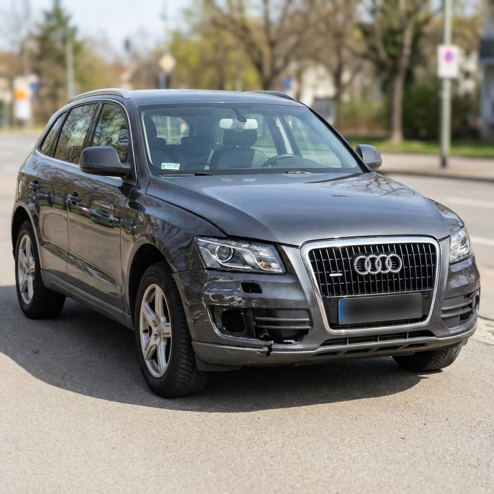Ein schwarzer Audi SUV mit sichtbarem Schaden am vorderen linken Stoßfänger steht am Straßenrand
